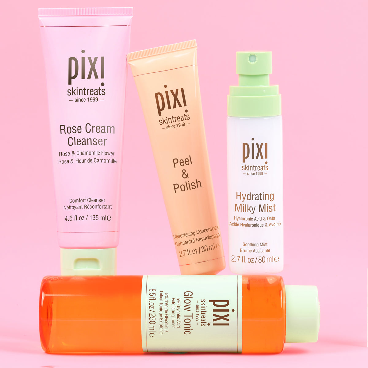 Pixi Glow Starter Routine skincare set arranged on a solid pink background: Rose Cream Cleanser in a pink tube, Peel & Polish in a peach tube, Hydrating Milky Mist in a white bottle with a mint cap, and Glow Tonic in an orange bottle with a pale green cap.