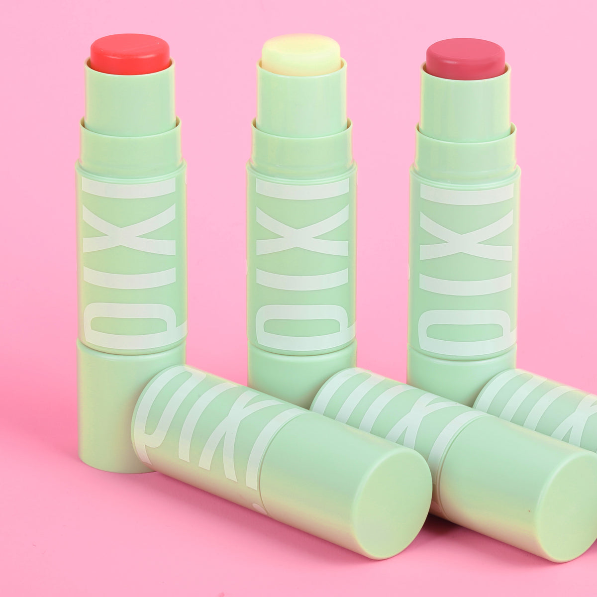 +Hydra LipTreat three product shades shown on pink background - additional product shown in the image to feature the cap on version.