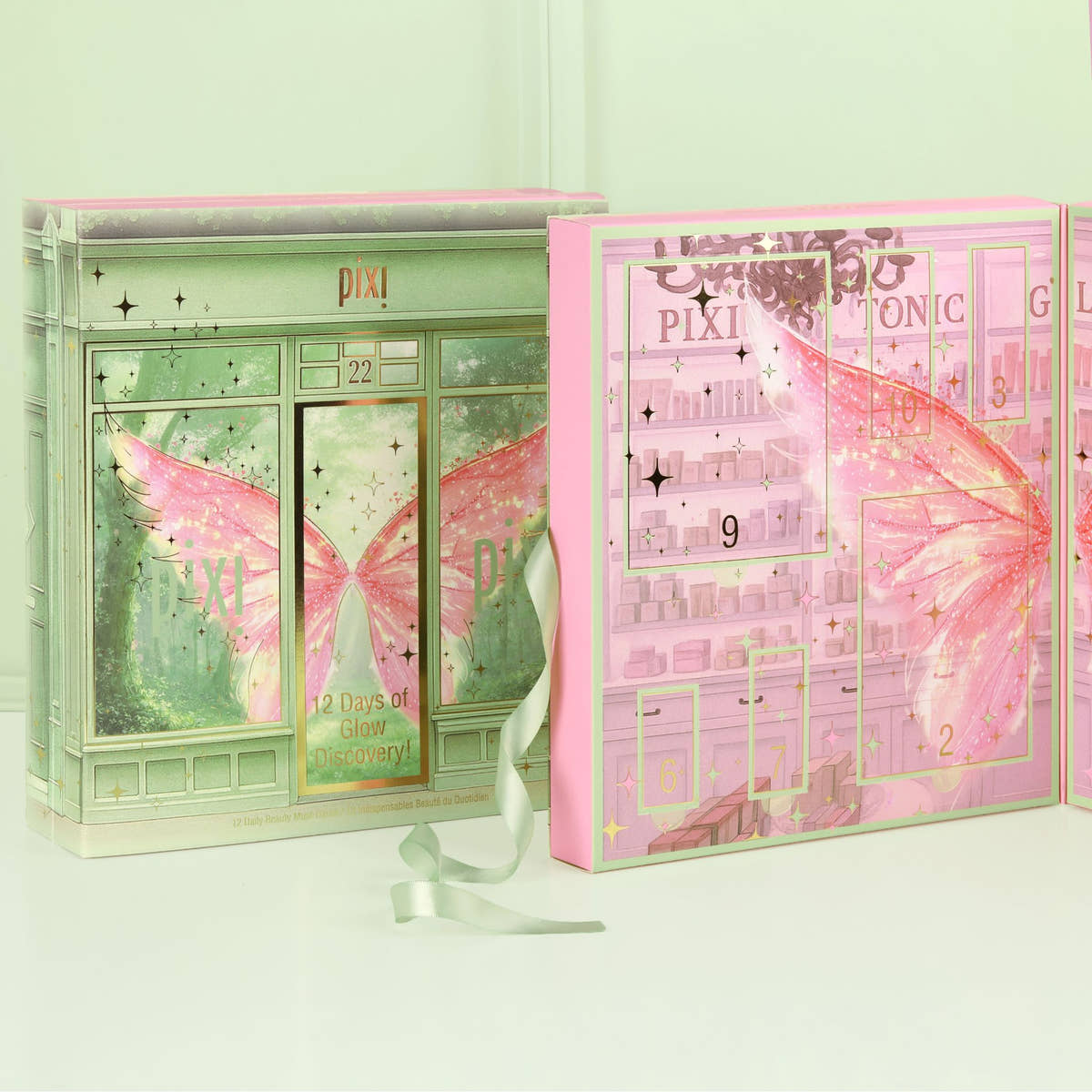 A pink and mint green Pixi advent calendar set displayed on a clean white surface against a pale mint green background. The left box shows the front design with a fairy shop storefront and butterfly wings, while the right box shows the back design with numbered compartments and a large pink butterfly wing graphic.