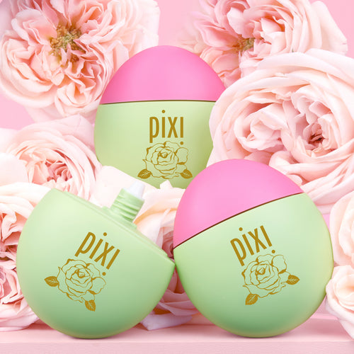 Three Pixi HandHero PixiRose scented products arranged among pink roses on a pink background. One cap is removed to show applicator tip. view 2